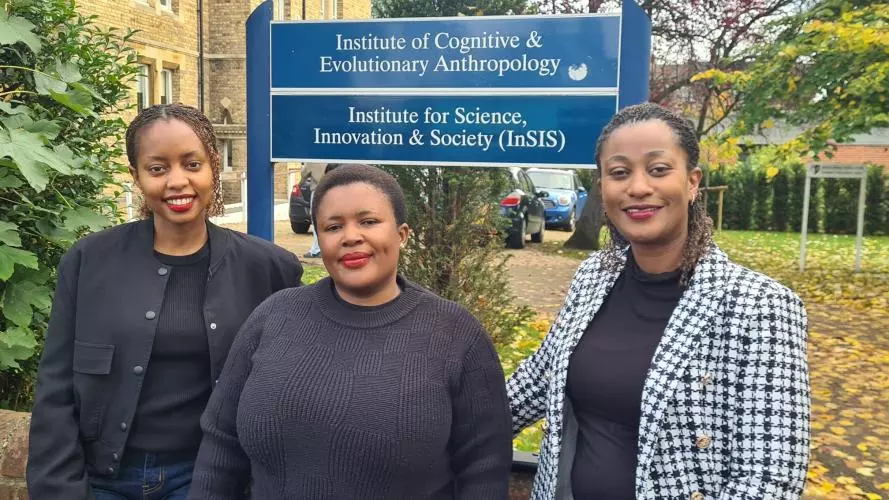 Three women standing in a line outside the department buildings, under a sign for the Institute for Science, Innovation and Society (InSIS)