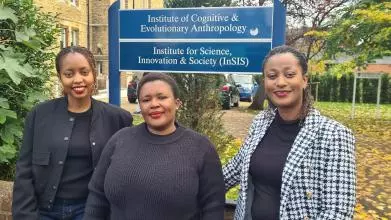 Three women standing in a line outside the department buildings, under a sign for the Institute for Science, Innovation and Society (InSIS)